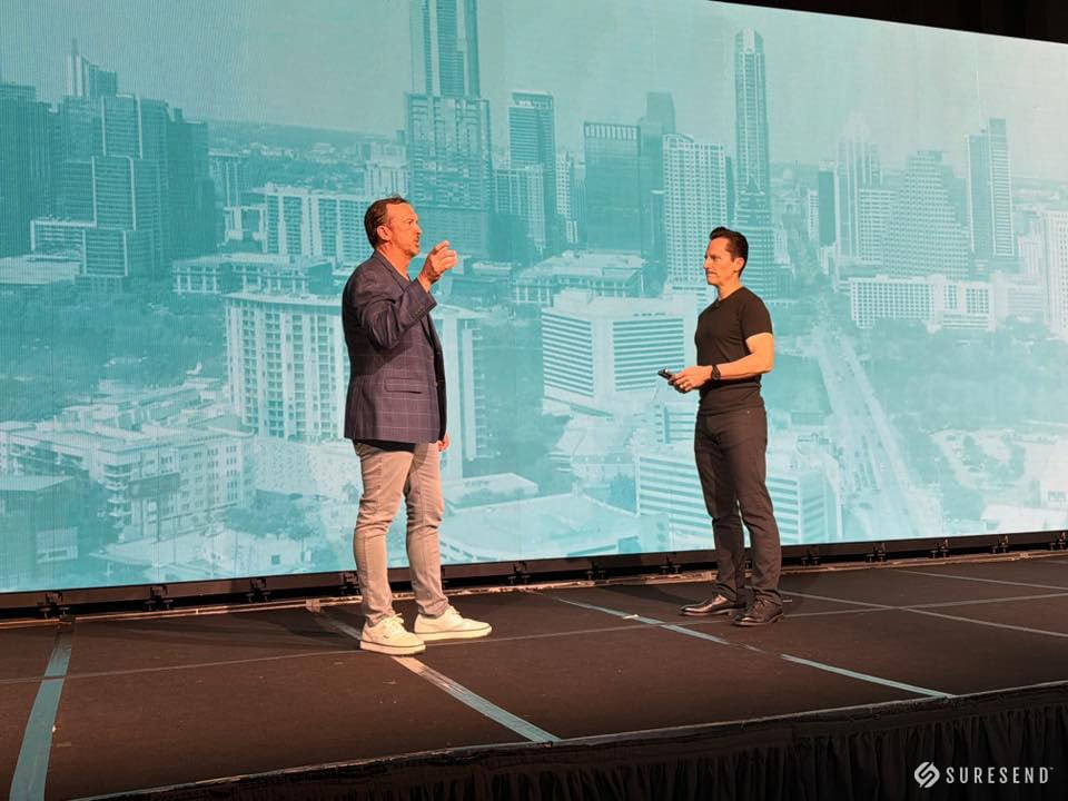 Sure Send CRM experts discuss solutions on stage, city skyline screen, branded logo; Resource Center event at learn.suresend.ai.
